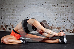 Woman sport stretching in gym with brick wall and black mats