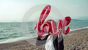 woman in sport wearing holding love air balloon letters on the beach