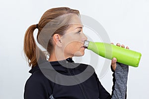 Woman in sportiv dress holding green thermos bottle drinking