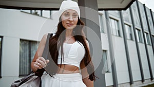 Woman in Sports Clothes with bag near the gym outdoors. Female Athlete Going to Training in Morning Gym Routine Before Work