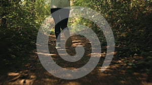 A woman in sports clothes runs through a summer forest. Legs close-up, rear view. In real time. The concept of a healthy