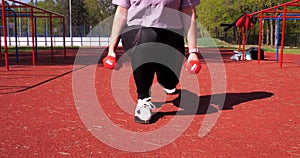 A woman on the sports ground makes a lunge with dumbbells in her hands. Workout in the park with dumbbells to strengthen