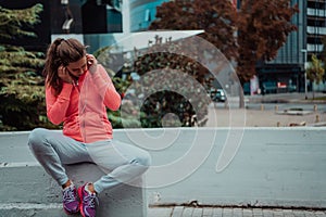 a woman in a sports outfit is resting in a city environment after a hard morning workout while using noiseless