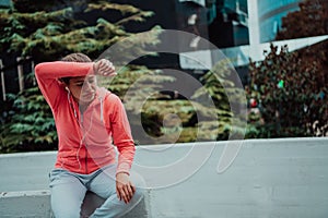 a woman in a sports outfit is resting in a city environment after a hard morning workout while using noiseless