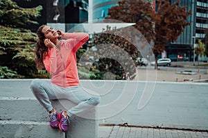 a woman in a sports outfit is resting in a city environment after a hard morning workout while using noiseless