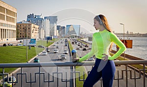 Woman in sportswear and a bottle of water stands on a bridge over a road with cars, buildings, sports girl in the city