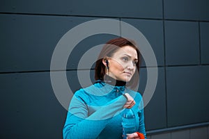 Woman in sportswear drinking clean water from a bottle during a workout on the street. Running, fitness, active healthy lifestyle