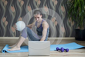 Woman in sportswear on the floor with ball and is using a laptop at home in the living room. Workout online concept