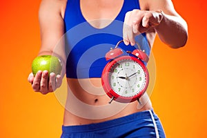Woman in sportswear holding alarm clock and apple. People, fitness and healthcare concept