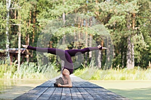 A woman in sportswear, practicing yoga in the park, on a mat performs a shirshasana exercise with a transverse twine, headstand