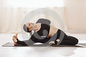 A woman in sportswear practicing yoga, sitting on a mat, performs the Parivrtta Janu Shirshasana exercise, head-to-knee posture