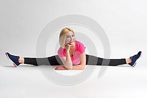 A woman in sportswear and sneakers sits in a transverse split