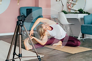 A woman in sportswear works out at home on a mat in front of a mobile phone.
