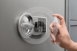 Woman spraying antiseptic onto keypad of safe, closeup