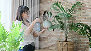 Woman spraying indoor plants at home using spray bottle with fertilized water