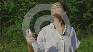 Woman spraying insect repellent on her face outdoor in nature using spray bottle