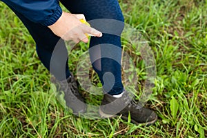 Woman spraying insect repellent at her legs. Woman using anti mosquito spray outdoors at hiking trip