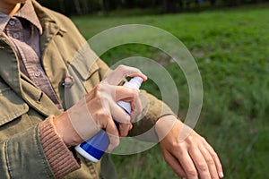 woman spraying insect repellent to hand at park