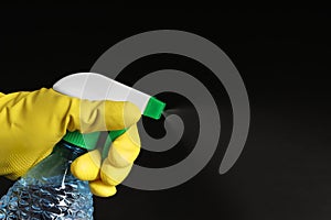 Woman spraying liquid from bottle on black background, closeup. Space for text