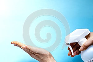 A woman sprays her hand with antiseptic from a plastic spray bottle. Hands with a bottle close-up on a blue background