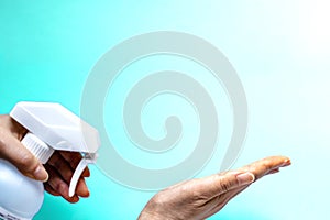 A woman sprays her hand with antiseptic from a plastic spray bottle. Hands with a bottle close-up on a blue green background