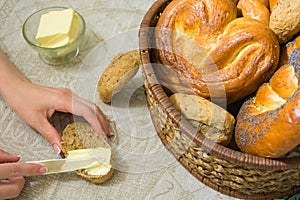 Woman spread the butter on the slice of bread and different bread in the basket