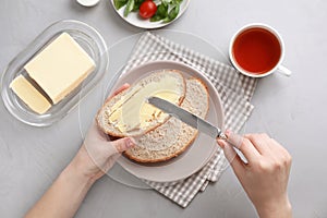 Woman spreading butter on slice of bread over table