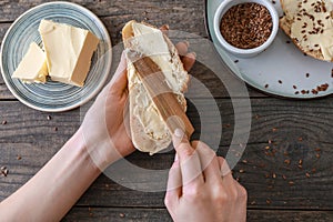 Woman spreading tasty butter onto slice of bread on wooden background