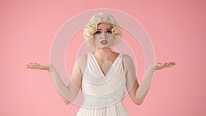 A woman spreads her hands in despair. A woman in the image of Marilyn Monroe in the studio on a pink background.