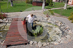 A woman in the spring cleans an artificial pond