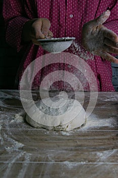 The woman sprinkles flour dough from the fullness for sifting flour, flour falls on the dough, a beautiful scattering of flour.