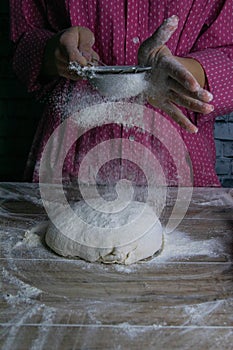 The woman sprinkles flour dough from the fullness for sifting flour, flour falls on the dough, a beautiful scattering of flour.