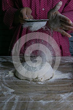 The woman sprinkles flour dough from the fullness for sifting flour, flour falls on the dough, a beautiful scattering of flour.