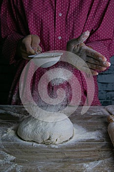 The woman sprinkles flour dough from the fullness for sifting flour, flour falls on the dough, a beautiful scattering of flour.