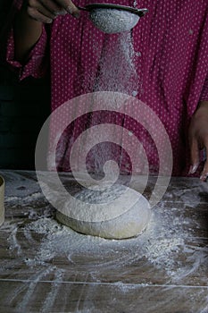 The woman sprinkles flour dough from the fullness for sifting flour, flour falls on the dough, a beautiful scattering of flour.