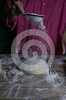 The woman sprinkles flour dough from the fullness for sifting flour, flour falls on the dough, a beautiful scattering of flour.