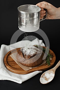 A woman sprinkles freshly baked bread with flour on a black background. Photogenic food