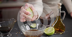 Woman squeezes fresh lime juice into teriyaki soy sauce in a glass bowl preparing marinade