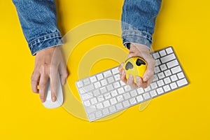 Woman squeezing antistress ball while working with computer on yellow background, top view