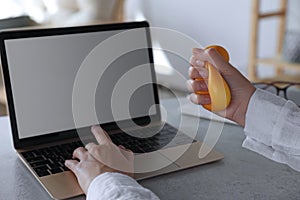 Woman squeezing antistress ball while working on laptop in office, closeup