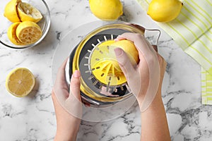 Woman squeezing lemon juice with reamer at white table, top view