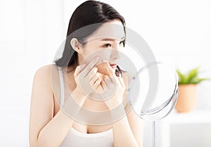 woman squeezing pimples in front of mirror
