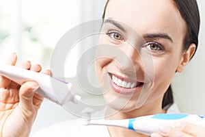 Woman Squeezing Toothpaste Onto Electric Toothbrush In Bathroom