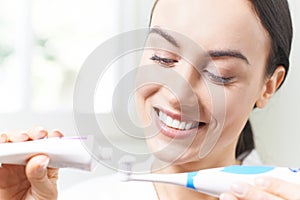 Woman Squeezing Toothpaste Onto Electric Toothbrush In Bathroom photo