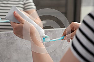 Woman squeezing toothpaste from tube onto toothbrush near mirror in bathroom, closeup