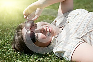 Woman squint from the bright sun, lie on green grass, city park, summer outdoor