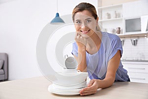 Woman with stack of clean dishes at kitchen table.