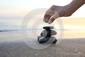 Woman stacking dark stones on sand near sea  for text