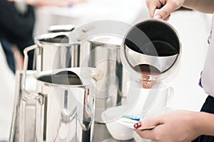 woman staff is pouring chocolate milk in pot to serve guests attending seminar during break time.