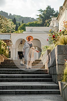 Woman on the stairs in the park. A middle-aged lady in a hat in a white outfit with a bag walks around the Livadia
